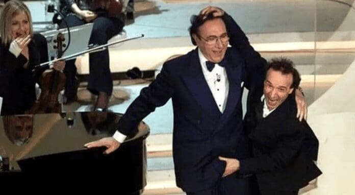 Enna, caso Rugolo, secondo la difesa… «Salutare toccando i genitali è pratica sdoganata» e in aula mostrano una foto di Baudo e Benigni